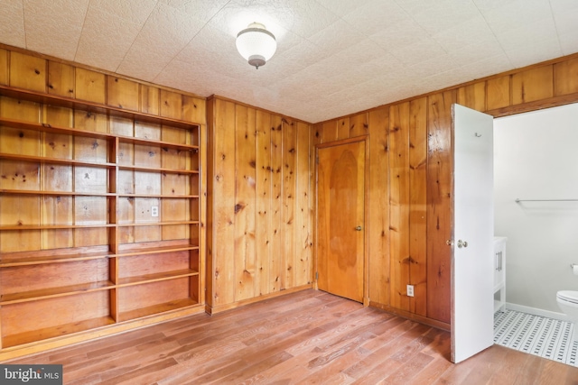 empty room featuring baseboards, wood finished floors, and wooden walls