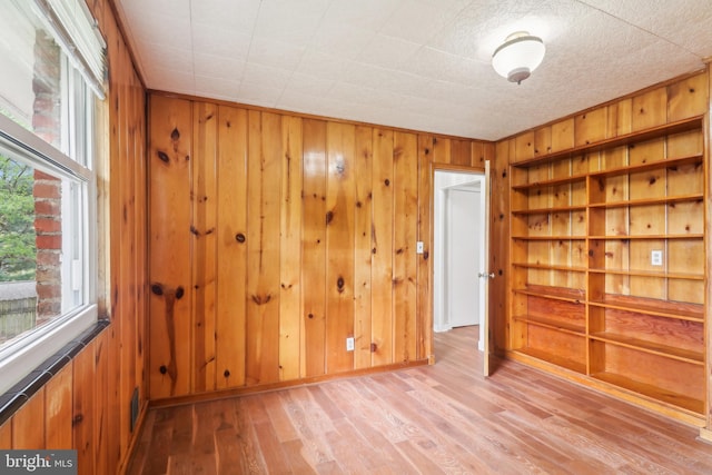 spare room with light wood-type flooring, wood walls, and built in shelves