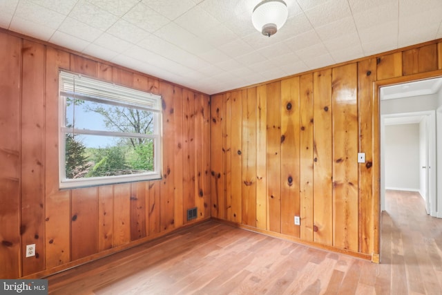spare room featuring wooden walls, visible vents, and light wood-style flooring
