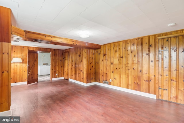 unfurnished room with wood finished floors, visible vents, wood walls, and baseboards
