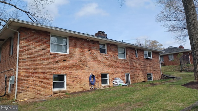 rear view of house with brick siding, a lawn, and a chimney