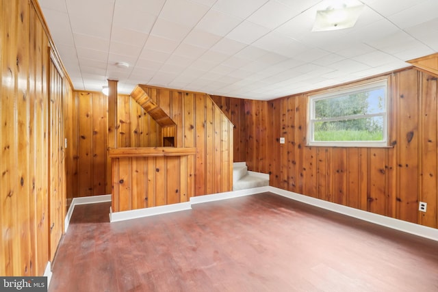 bonus room featuring baseboards, wood finished floors, wood walls, and stairs