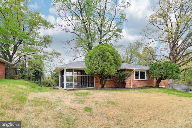 back of house featuring brick siding, a sunroom, fence, and a lawn