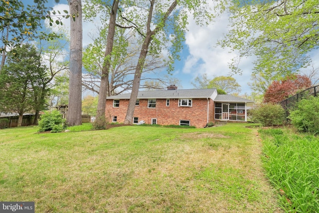 back of property with a chimney, fence, a yard, brick siding, and a sunroom