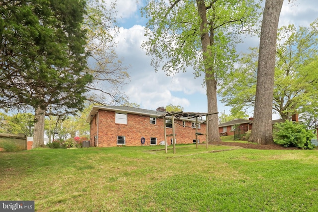 rear view of house featuring a chimney, brick siding, a yard, and central AC unit