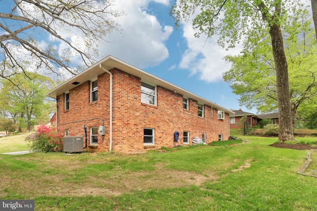 view of side of home featuring brick siding, a yard, and central air condition unit