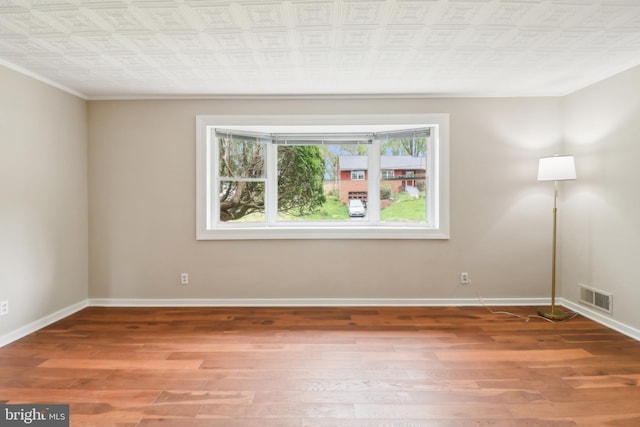 spare room with an ornate ceiling, baseboards, visible vents, wood finished floors, and ornamental molding