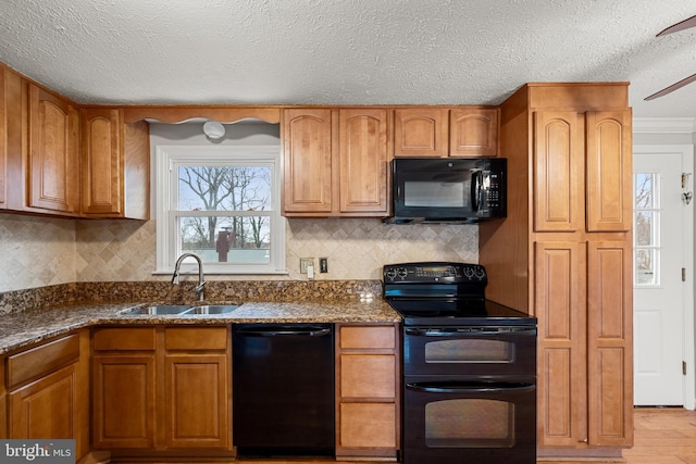 kitchen featuring sink, light hardwood / wood-style flooring, dark stone countertops, backsplash, and black appliances