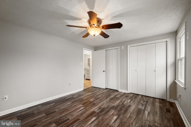 unfurnished bedroom featuring multiple closets, ceiling fan, dark hardwood / wood-style flooring, and a textured ceiling