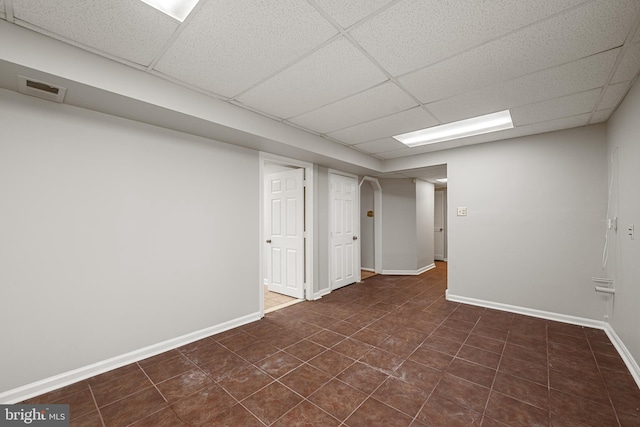 basement featuring dark tile patterned floors and a drop ceiling