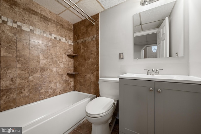 full bathroom with a paneled ceiling, tile patterned flooring, tiled shower / bath combo, vanity, and toilet