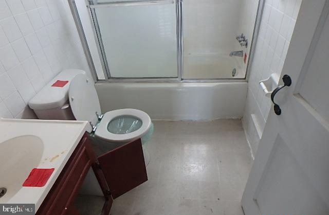 full bathroom featuring vanity, toilet, combined bath / shower with glass door, and tile walls