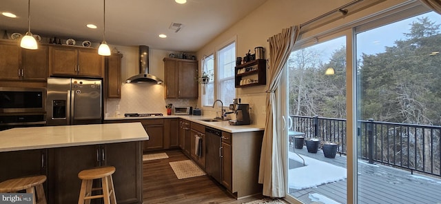 kitchen featuring wall chimney range hood, sink, appliances with stainless steel finishes, hanging light fixtures, and dark hardwood / wood-style floors