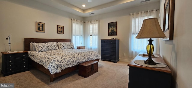 carpeted bedroom featuring a tray ceiling and multiple windows