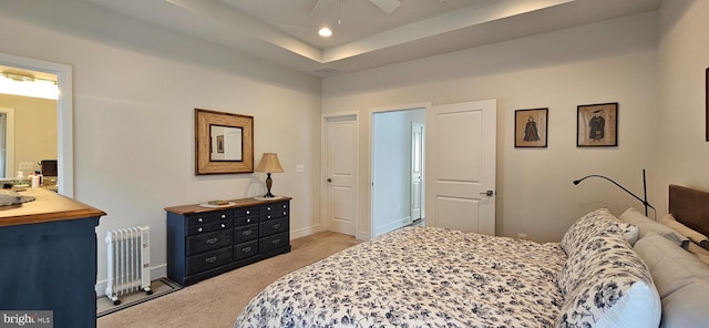 bedroom with a raised ceiling, radiator heating unit, light colored carpet, and ceiling fan