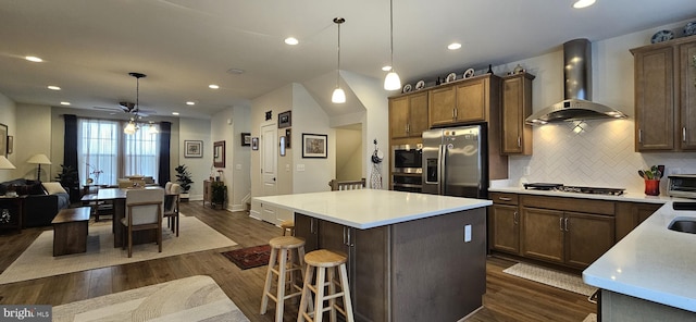 kitchen with pendant lighting, dark hardwood / wood-style flooring, wall chimney exhaust hood, and appliances with stainless steel finishes