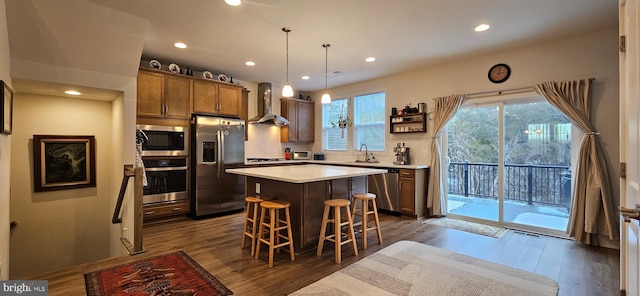 kitchen featuring pendant lighting, sink, stainless steel appliances, a center island, and wall chimney exhaust hood