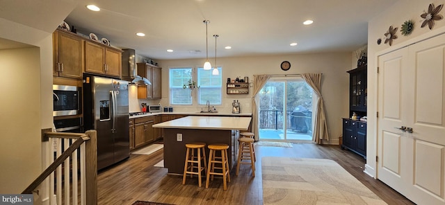 kitchen featuring a kitchen bar, sink, a center island, stainless steel appliances, and wall chimney range hood