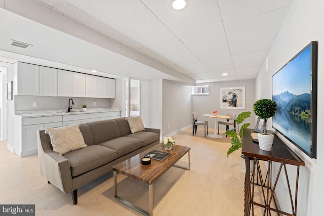 living room featuring sink, a paneled ceiling, and light wood-type flooring