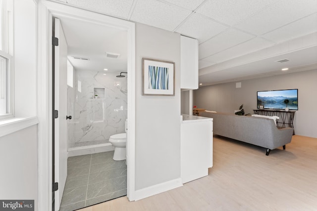 bathroom featuring a paneled ceiling, wood-type flooring, toilet, and a tile shower