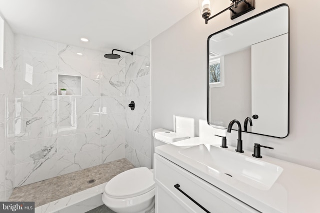 bathroom with tiled shower, vanity, and toilet