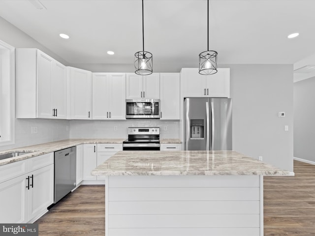 kitchen with appliances with stainless steel finishes, decorative light fixtures, white cabinets, a center island, and light stone counters