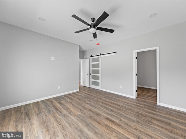 unfurnished bedroom featuring a walk in closet, a barn door, dark hardwood / wood-style floors, and ceiling fan