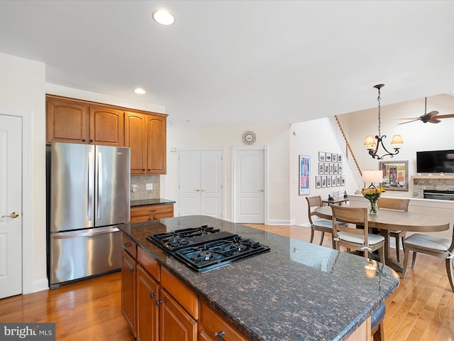 kitchen with hanging light fixtures, stainless steel refrigerator, a kitchen island, black gas cooktop, and light hardwood / wood-style floors