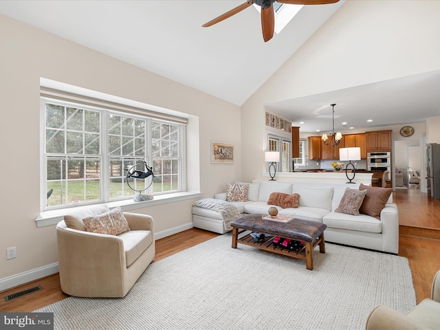 living room featuring high vaulted ceiling, ceiling fan with notable chandelier, and light wood-type flooring