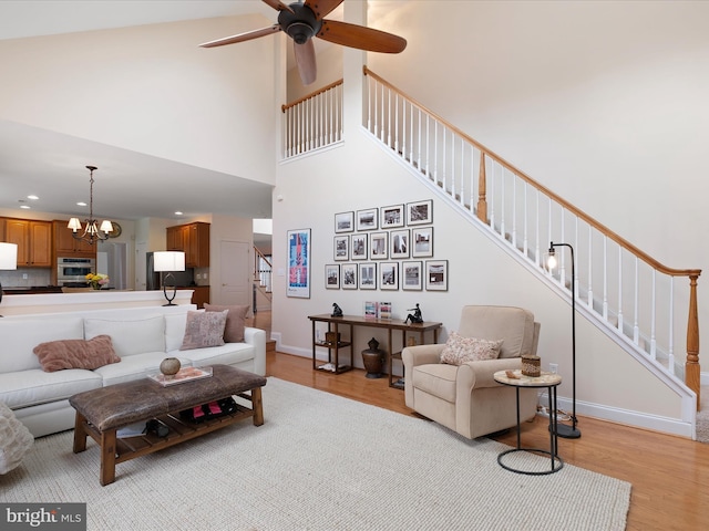 living room with a towering ceiling, ceiling fan with notable chandelier, and light wood-type flooring