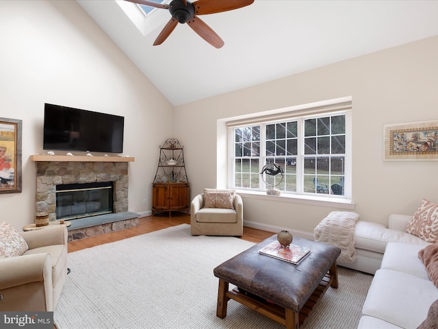 living room with wood-type flooring, ceiling fan, a fireplace, and a skylight