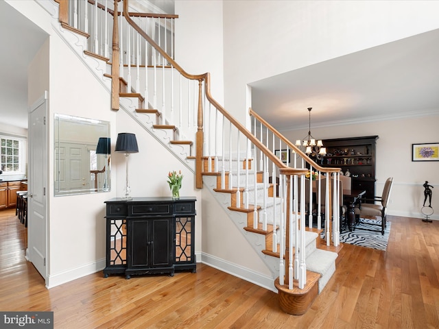 staircase featuring an inviting chandelier, ornamental molding, hardwood / wood-style floors, and a high ceiling