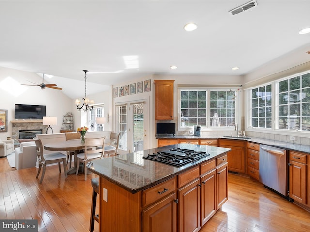 kitchen with a stone fireplace, a center island, hanging light fixtures, stainless steel dishwasher, and black gas stovetop