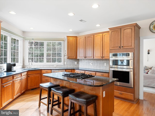 kitchen featuring sink, appliances with stainless steel finishes, a kitchen breakfast bar, a kitchen island, and dark stone counters