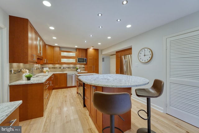 kitchen with a breakfast bar, sink, a center island, stainless steel appliances, and light stone countertops