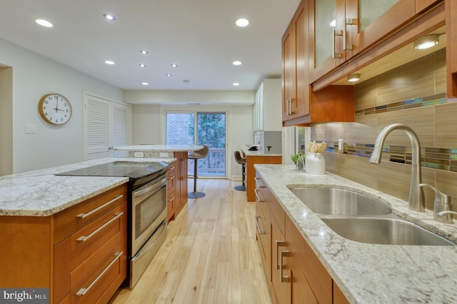 kitchen featuring sink, stainless steel range with electric cooktop, light stone counters, a kitchen island, and backsplash