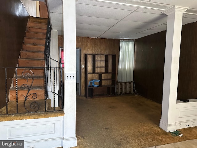 interior space featuring carpet floors, wooden walls, and a paneled ceiling