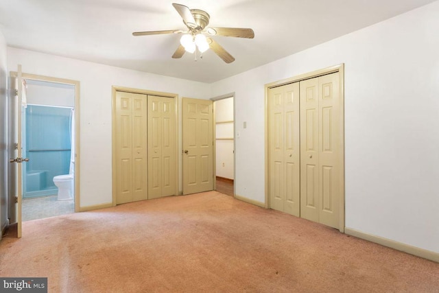 unfurnished bedroom featuring ceiling fan, two closets, light colored carpet, and ensuite bath