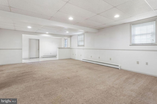 basement featuring a baseboard radiator, a healthy amount of sunlight, and light colored carpet