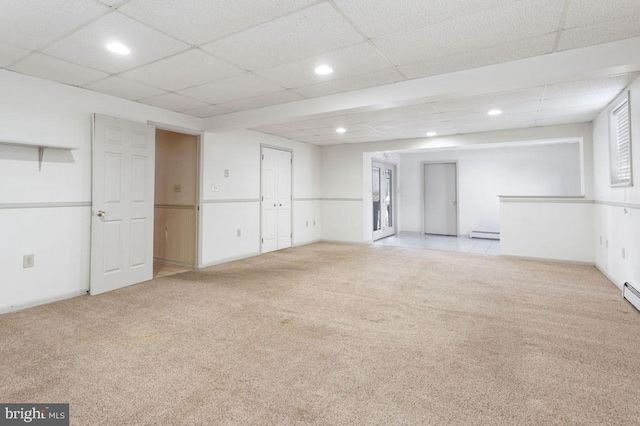 basement featuring light carpet, a baseboard heating unit, and a paneled ceiling