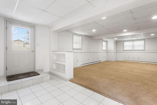 basement with baseboard heating, light carpet, and a drop ceiling