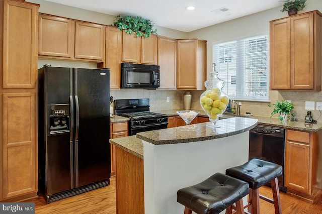 kitchen with a breakfast bar area, decorative backsplash, light stone counters, black appliances, and light wood-type flooring