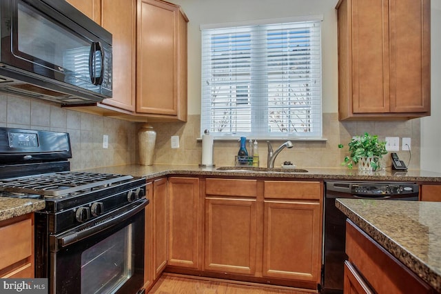 kitchen featuring light stone counters, sink, backsplash, and black appliances