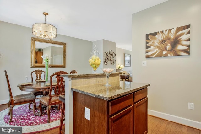 kitchen with hanging light fixtures, light stone countertops, a center island, and light wood-type flooring