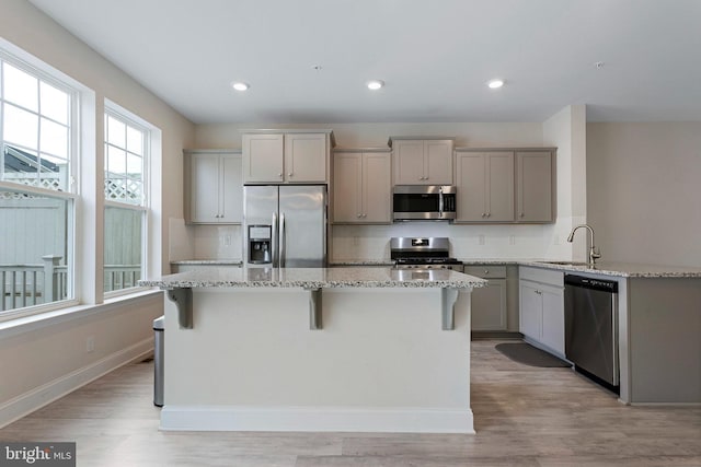 kitchen with sink, gray cabinets, a breakfast bar area, stainless steel appliances, and light stone countertops