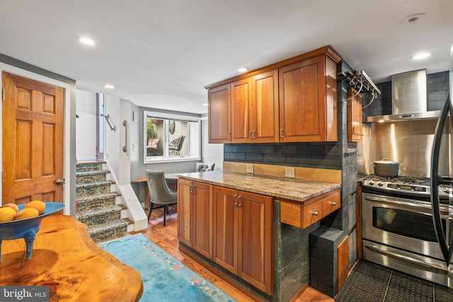 kitchen featuring decorative backsplash, hardwood / wood-style flooring, gas range, light stone countertops, and wall chimney exhaust hood