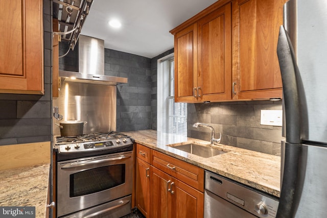 kitchen with stainless steel appliances, light stone countertops, sink, and wall chimney range hood