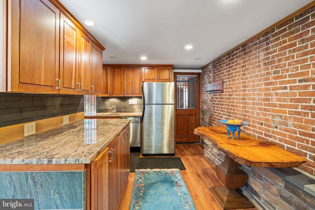 kitchen with stainless steel fridge, light stone counters, tasteful backsplash, light hardwood / wood-style floors, and brick wall