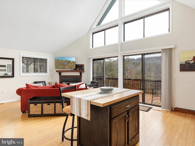 kitchen featuring a kitchen island, dark brown cabinets, high vaulted ceiling, and light hardwood / wood-style floors