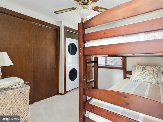 bedroom featuring stacked washing maching and dryer, light colored carpet, and ceiling fan